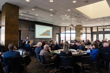 Photo of attendees at roundtable meeting sitting at tables with Prof. Sally Benson opening the meeting.