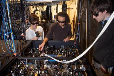 Monika Schleier-Smith (at center with graduate students Emily Davis and Eric Cooper) uses laser-cooled atoms in her lab at Stanford to study the transfer of quantum information. (Dawn Harmer/SLAC National Accelerator Laboratory)   