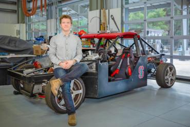 Photo of John Alsterda in front on the X1 research vehicle at the Automotive Innovation Facility