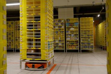 Photo of Amazon fulfillment center where a robot carries orders in the stacked yellow shelving system.