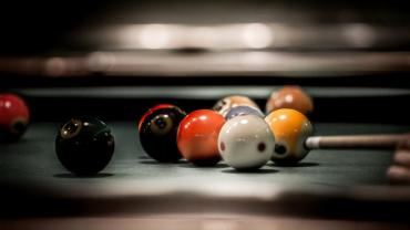 Stylized photo of cue stick hitting billiards