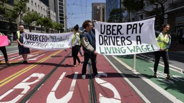 Photo of workers striking and holding a sign which reads, "Uber, Pay Drivers a Living Wage"