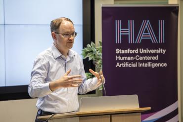 Photo of Prof Mykel Kochenderfer presenting adjacent to HAI sign
