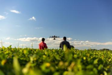 Photo of field with two people controlling a drone in the sky.