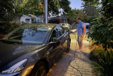 Photo of man charging EV in the driveway of home.