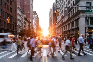 Photo of busy sidewalk in city between two tall buildings and sunset in background