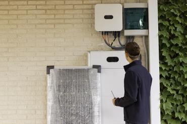 Photo of a person standing in front of a solar panel which is next to a home battery system