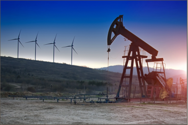 Photo of oil rig in foreground with wind turbines on the horizon.