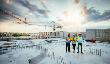 Photo of 3 people at a construction site with cranes in background and buildings being built