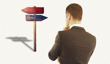 Image of the back of a man dressed in a suit looking at a sign post with arrows pointed in opposite directions