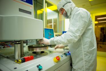 Photo of research loading a snall chip into the reactive ion etcher (RIE) at the nanopatterning Cleanroom in the Stanford Nano Shared Facilities.