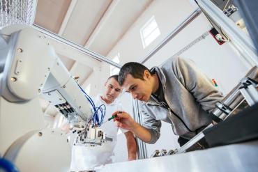Photo of two men working on a robotic arm.