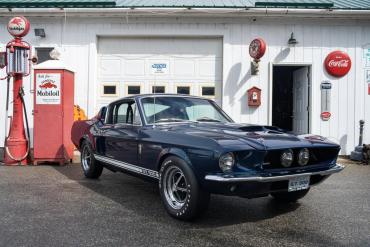 Photo of a navy blue Ford Mustang in front of an old-fashioned service station