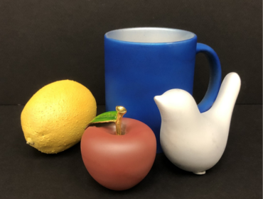 Still photo of blue mug in background with lemon, apple and ceramic white bird in foreground