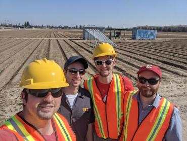 Co-founders wearing hardhats and vests in foreground of an agricultural field