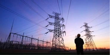 Photo of person looking up at transformers and transmission lines in the sunset