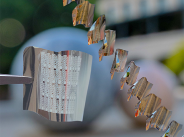 A flexible phase-change memory substrate held by tweezers (left) with a diagonal sequence showing substrates in the process of being bent. (Credit: Crystal Nattoo)