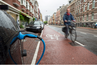 Photo of roadside with cars parked and charging with biker riding by