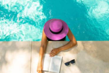 Photo of a woman in the pool at poolside reading a book