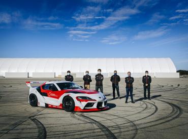 Photo of researchers around a Toyota autonomous drifting Supra at the racetrack.